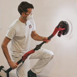 Man sanding a wall in preparation for painting it.